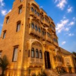 hotels near patwon ki haveli - Hotel Narpatgarh Palace Jaisalmer Ornate hotel facade with carved arches and balconies, warm lighting, under a blue sky at dusk.