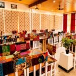 Colorful dining room with white wooden chairs covered in patchwork fabric and tiled tables in a sunlit cafe.](https://)